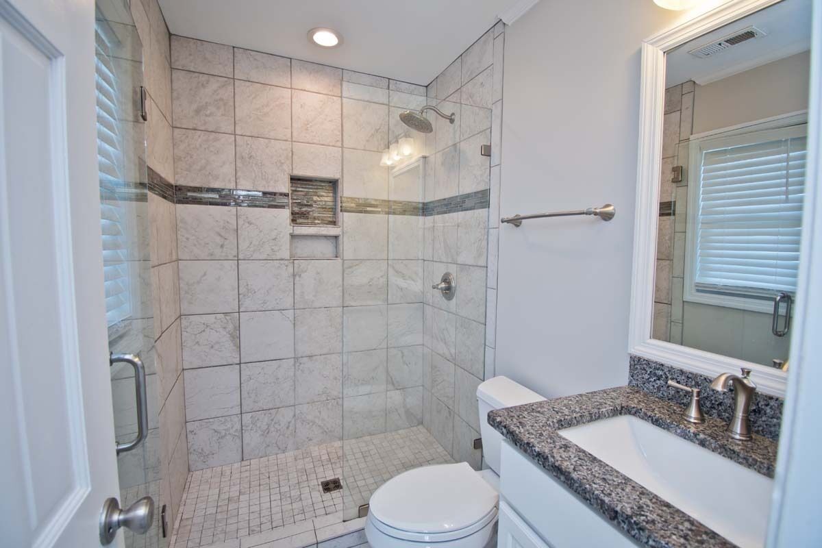 Een moderne badkamer met een inloopdouche, toilet en een wastafel met granieten blad.
