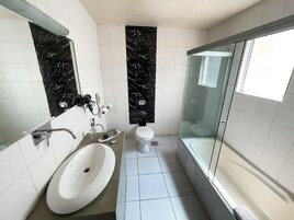 Un baño moderno con lavamanos blanco, inodoro y zona de ducha con mampara de vidrio.