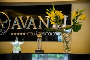 Una recepción con un letrero que dice "AVANI HOTEL & CONVENTION CENTER", un premio con forma de estrella y un florero con flores amarillas.