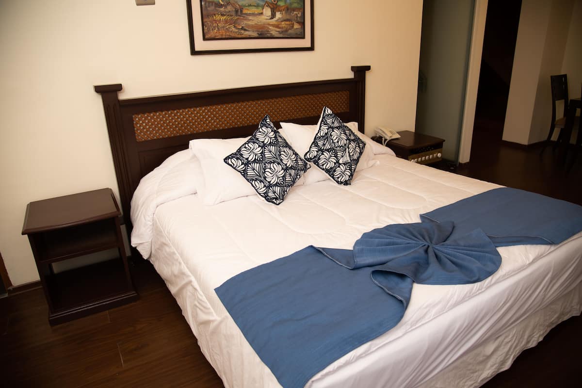 A neatly made bed with a blue and white patterned pillow, a blue throw, and a wooden headboard.