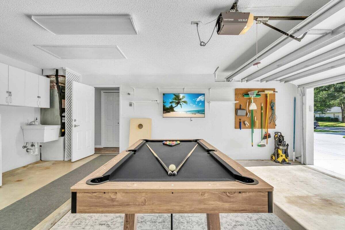 Une table de billard dans une pièce moderne, avec une grande fenêtre, un téléviseur fixé au mur et un panneau perforé où sont rangés des outils.