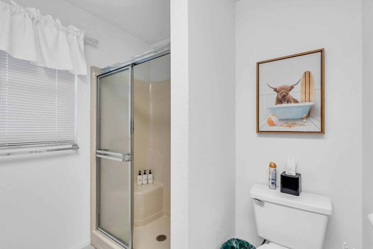 Een badkamer met een douchecabine van glas, een toilet en een ingelijst foto van een hond in bad.