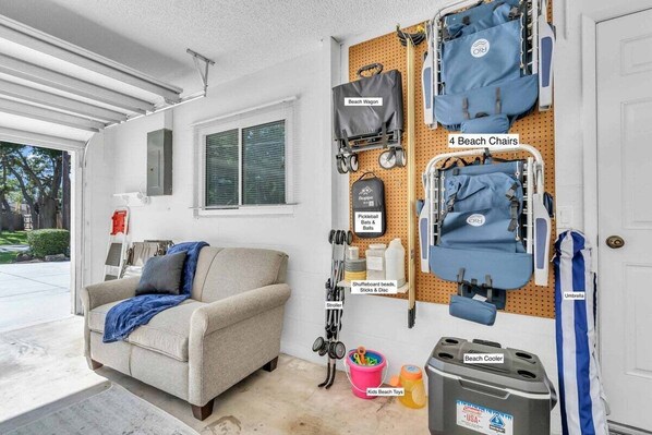 A garage with a pegboard wall displaying beach-related items like beach chairs, a beach wagon, and a beach cooler.