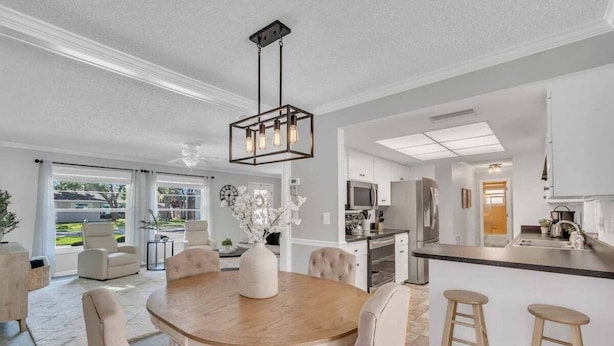 A modern kitchen with a central island, a dining area with a round table, and a view of the outdoors through large windows.