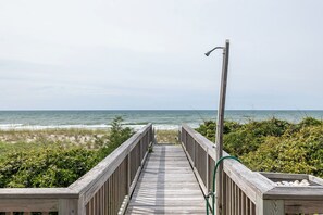 Une promenade en bois menant à la plage, avec une rambarde en métal et un tuyau d’arrosage sur la droite.