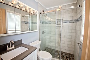 Une salle de bain avec une douche à parois de verre, un lavabo doté d’un robinet moderne et des toilettes.