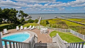 A pool area with a view of the water, deck chairs, and a wooden deck. - Witt's Inn, Soundfront House in Emerald Isle, NC! (Emerald Isle)