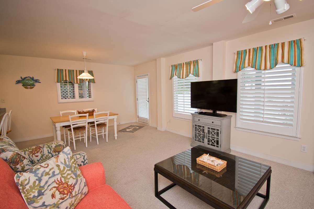 A living room with a sofa, coffee table, TV, dining table, chairs, and a ceiling fan.
