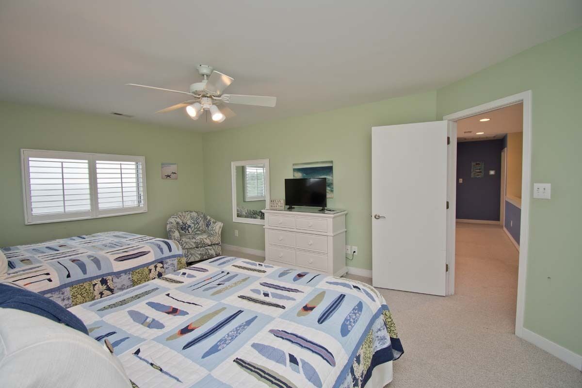 A bedroom with two beds, a dresser, a television, and a ceiling fan.