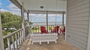 A covered porch with a swing, red chairs, and a view of the water. - Witt's Inn, Soundfront House in Emerald Isle, NC! (Emerald Isle)