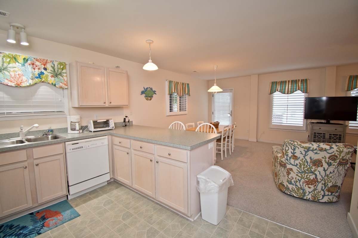 A compact kitchen with a dishwasher, microwave, and a small dining area with a chair.