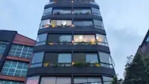 Un edificio de varios pisos con un diseño arquitectónico moderno, que cuenta con balcones con plantas y una serie de luces circulares en la entrada.