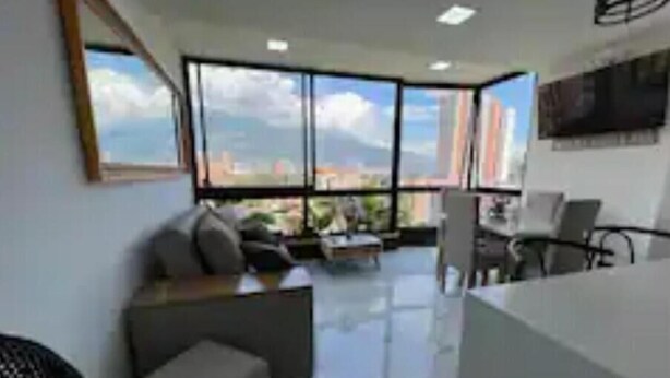 Una sala de estar moderna con un ventanal grande, un sofá, una mesa de centro y un televisor montado en la pared.