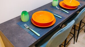 A dining table set with orange plates, green glassware, and blue cutlery.