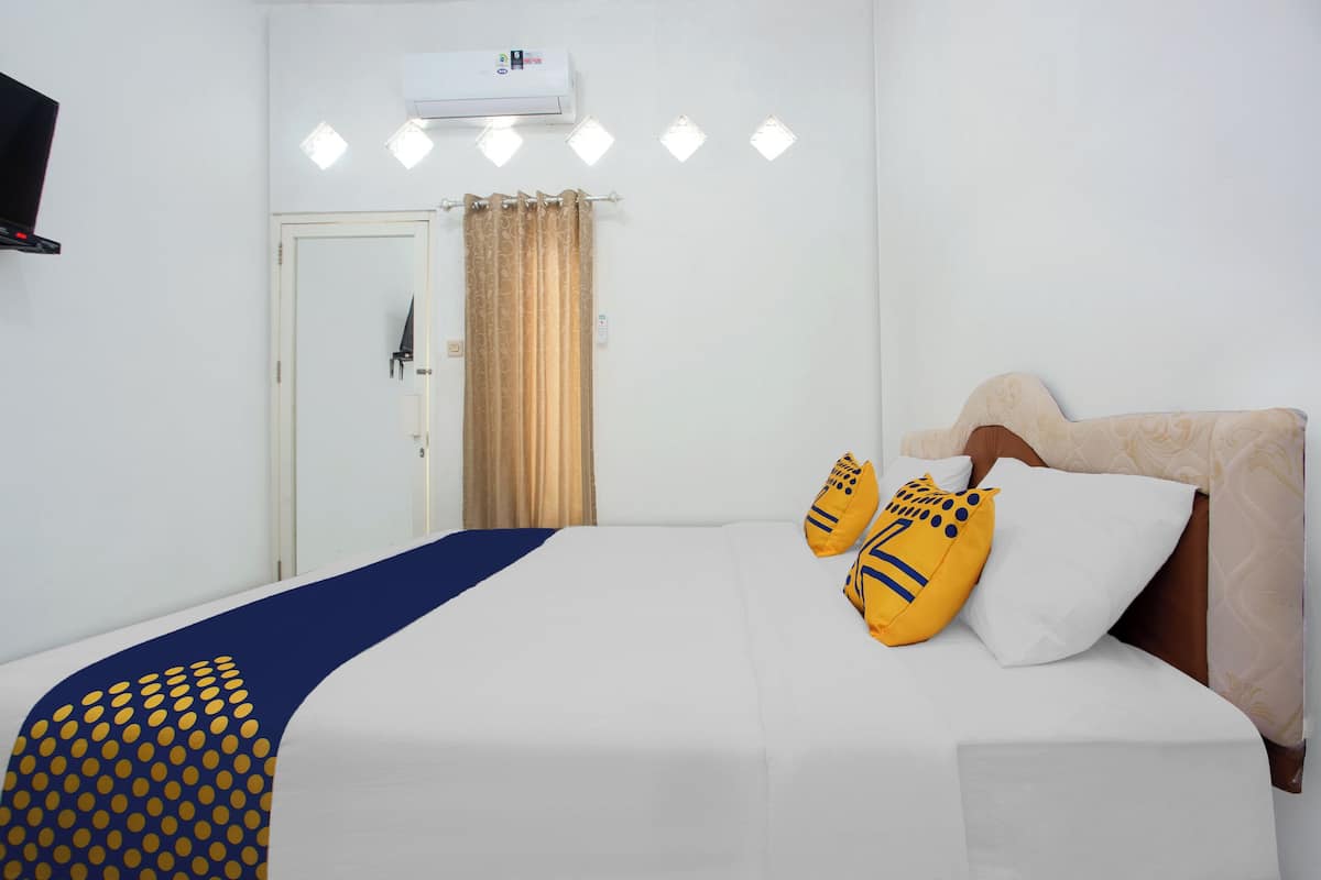 A hotel room with a bed, a TV, an air conditioner, and a curtain.