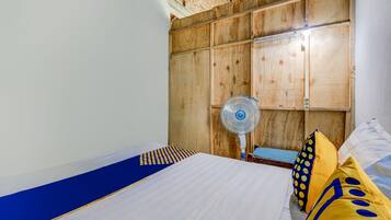 A bedroom with a wooden headboard, a bed with white bedding, and a blue and yellow patterned pillow.