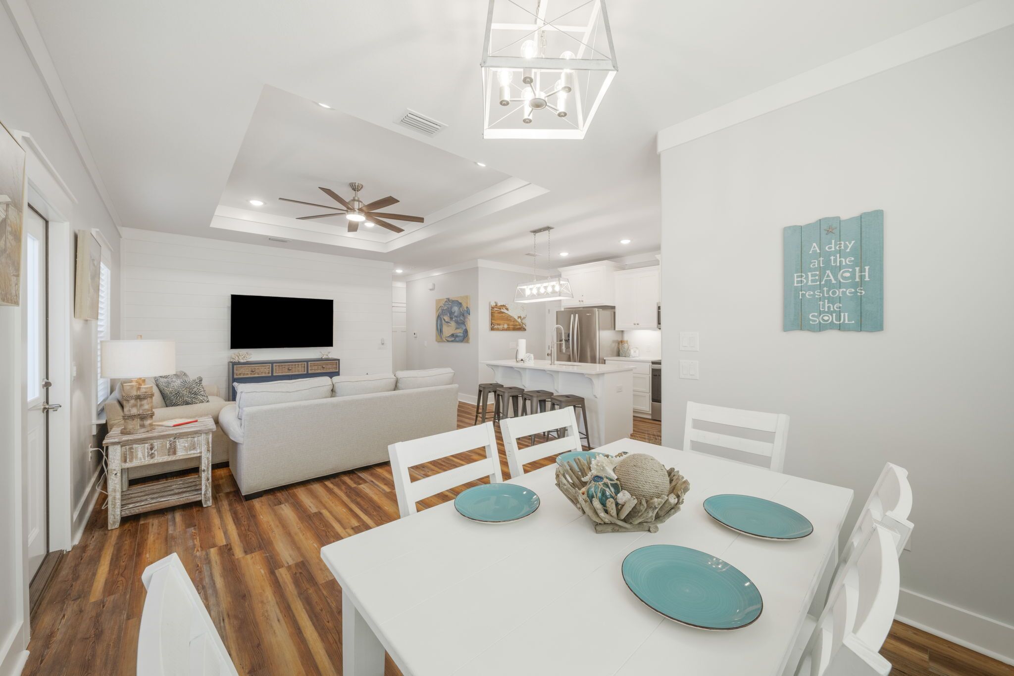 A modern living room with a white sofa, a dining table with blue plates, and a kitchen in the background.