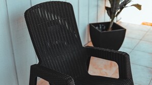 Un fauteuil à bascule en osier noir se trouve dans une pièce aux murs blancs et au sol carrelé.