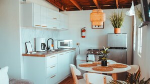 Une cuisine moderne avec des meubles blancs, un four à micro-ondes, une machine à café et une cuisinière. On y trouve une table à manger avec des sets de table en fibres tressées et des chaises.