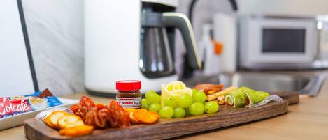 A wooden tray with snacks and a jar of Nutella, a microwave, and a coffee maker in a kitchen.