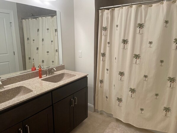 Bathroom features a large mirror, two sinks, and a shower with a palm tree patterned curtain.