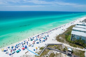 Une vue aérienne d’une plage où l’on voit de nombreux parasols et des personnes se prélassant au soleil.