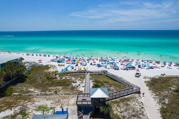 An aerial view of a beach with a wooden boardwalk leading to a building with a blue roof.