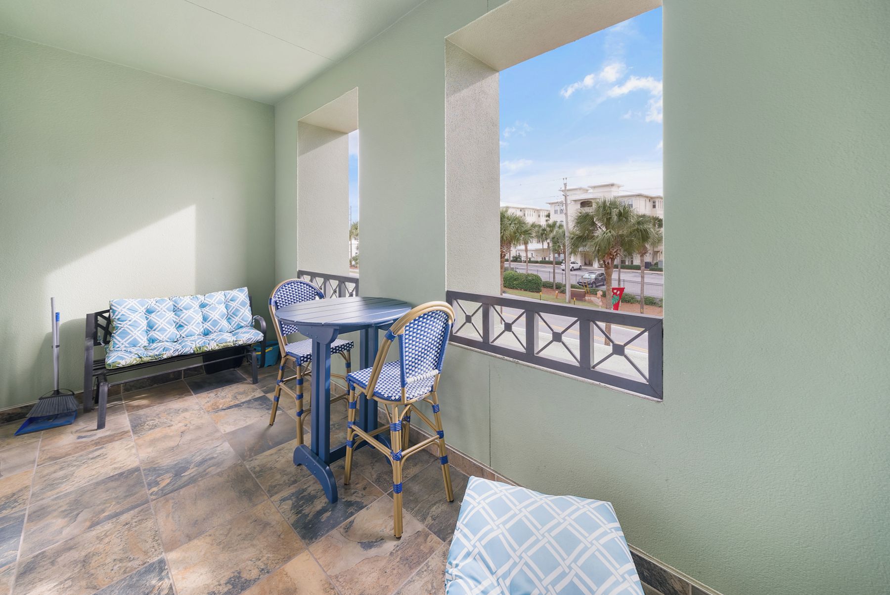 A balcony with a table and chairs, a sofa, and a view of buildings and palm trees.