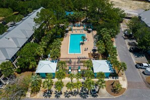 An aerial view of a resort with a central swimming pool, surrounded by palm trees and lounge chairs.