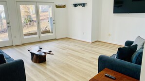 Una sala de estar con piso de madera, un sofá azul, una mesa de centro y un televisor montado en la pared.