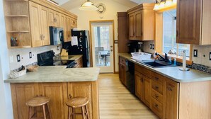Una cocina moderna con armarios de madera, una isla central con taburetes, un refrigerador negro y vistas al exterior.