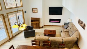 Una sala de estar con una mesa de comedor de madera, sofás y un televisor fijado en la pared.