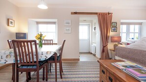 A room with a dining table, chairs, a bed, a dresser, and a window.