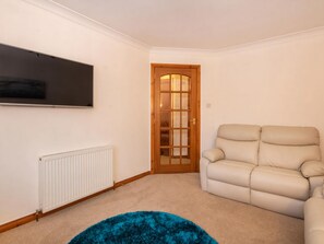 A room with a beige sofa, a blue rug, a white radiator, and a wooden door. - 2 bedroom accommodation in Inverness (Inverness)