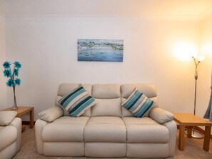 A beige sofa with striped pillows, a small wooden table, a tall floor lamp, and a painting of a coastal scene on the wall. - 2 bedroom accommodation in Inverness (Inverness)