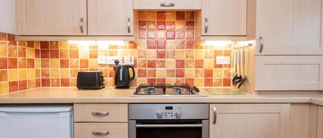 A kitchen with wooden cabinets, a gas stove, an oven, a toaster, and a kettle.