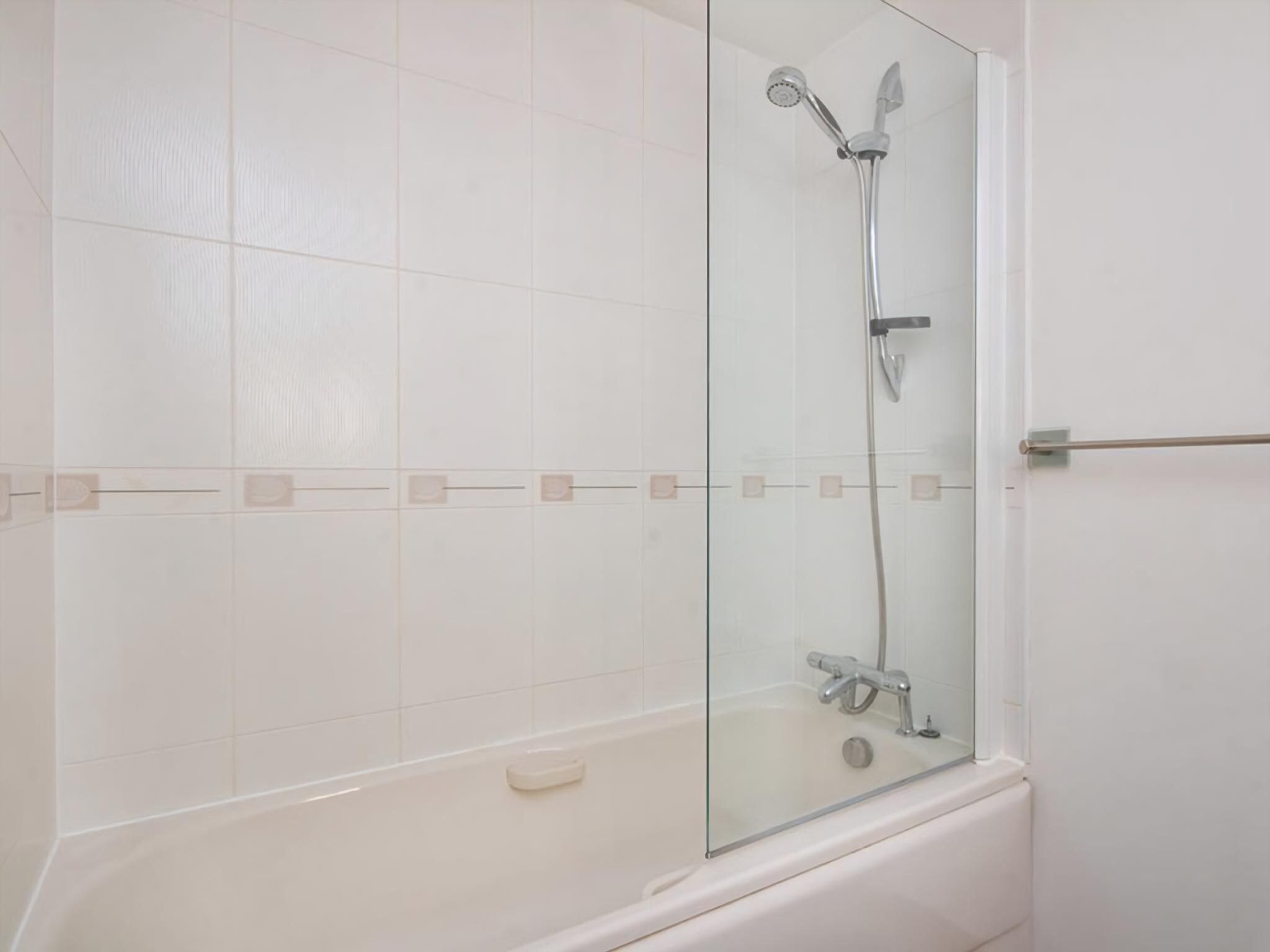 Une salle de bain avec une douche à parois de verre, une baignoire et des murs recouverts de carreaux blancs.