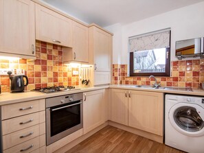 A modern kitchen with wooden cabinets, a gas stove, an oven, a washing machine, and a window with a view. - 2 bedroom accommodation in Inverness (Inverness)