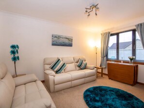 A living room with a beige sofa, a blue rug, a painting of a coastal scene, and a window with curtains. - 2 bedroom accommodation in Inverness (Inverness)