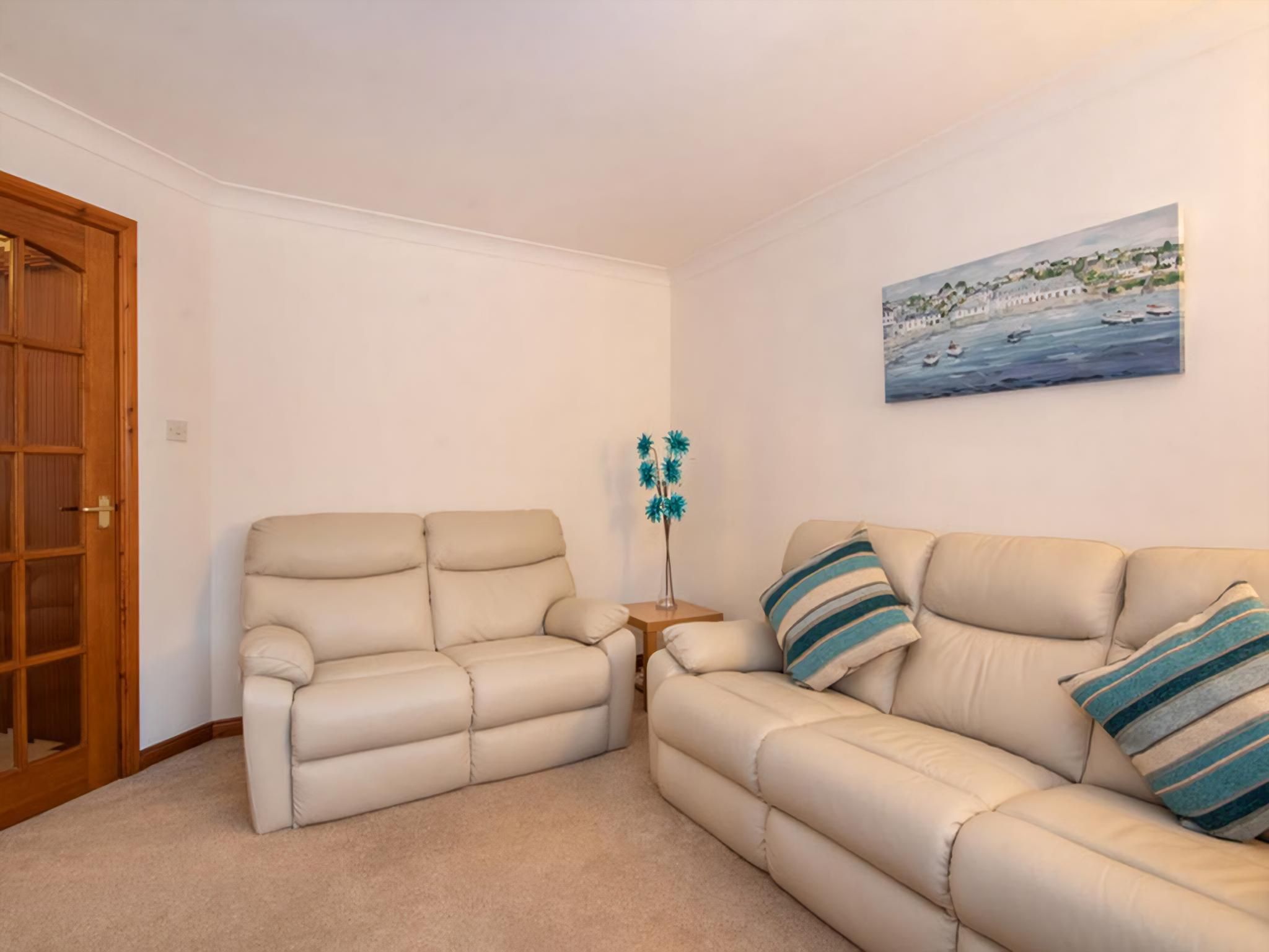 A living room with a beige sofa, a wooden door, and a painting of a coastal scene.