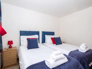 A hotel room with two beds, each with blue and red pillows, white linens, and a red lamp on a wooden nightstand. - 2 bedroom accommodation in Inverness (Inverness)