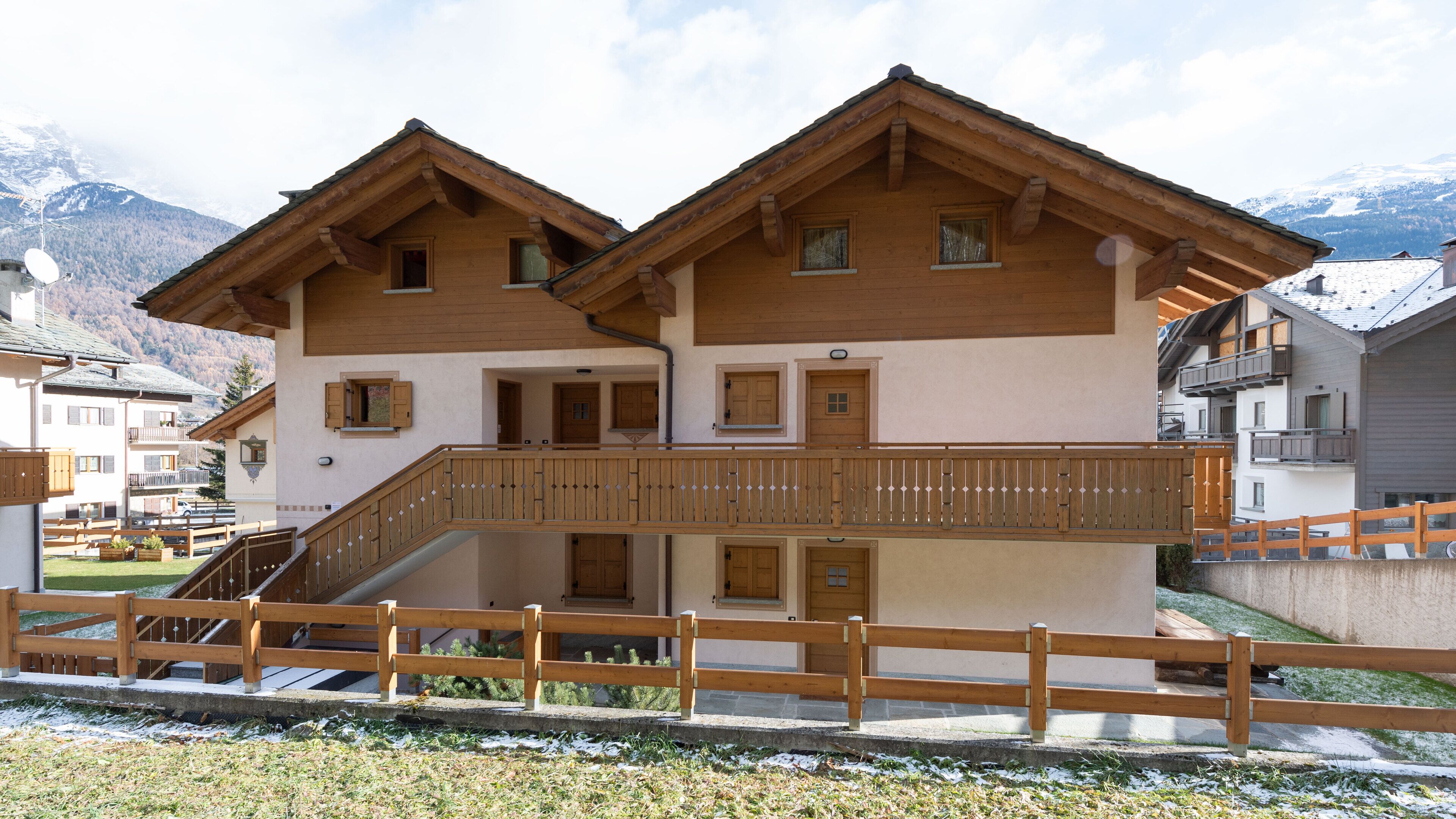 Un chalet de madera de dos pisos con balcón, una escalera y vista a montañas nevadas.
