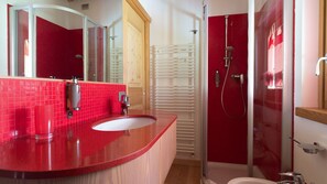 Een moderne badkamer met een rode wand betegeld, een houten wastafelmeubel, een glazen douchecabine en een witte badkuip.