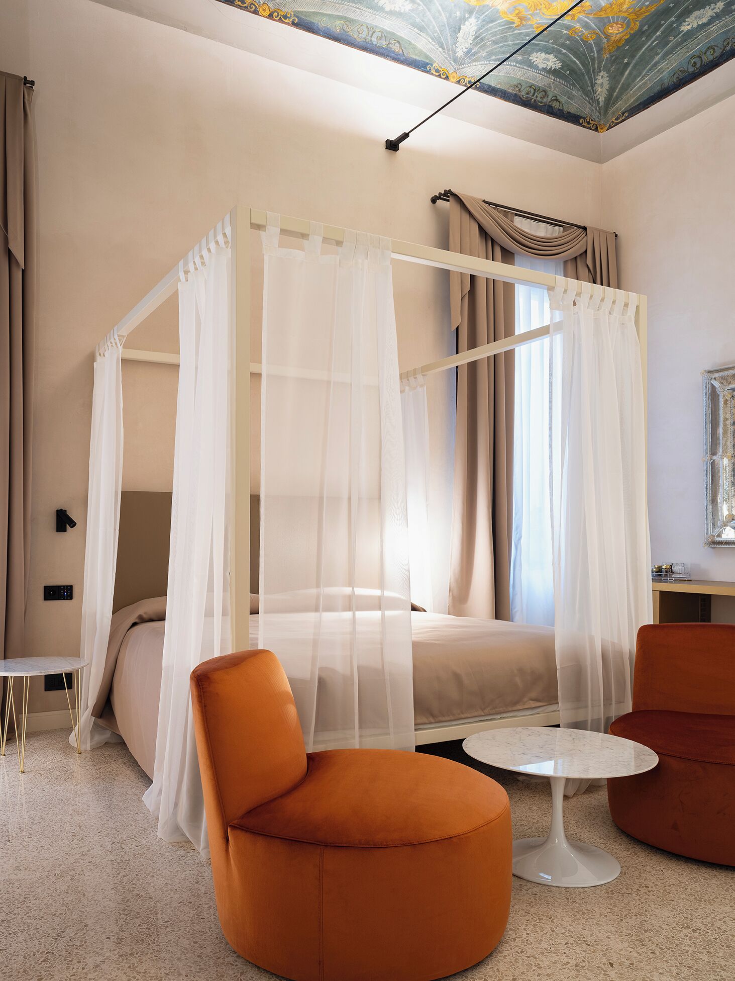 Un dormitorio moderno con una cama con dosel, dos sillones naranjas, una mesita redonda y un techo con diseño decorativo.