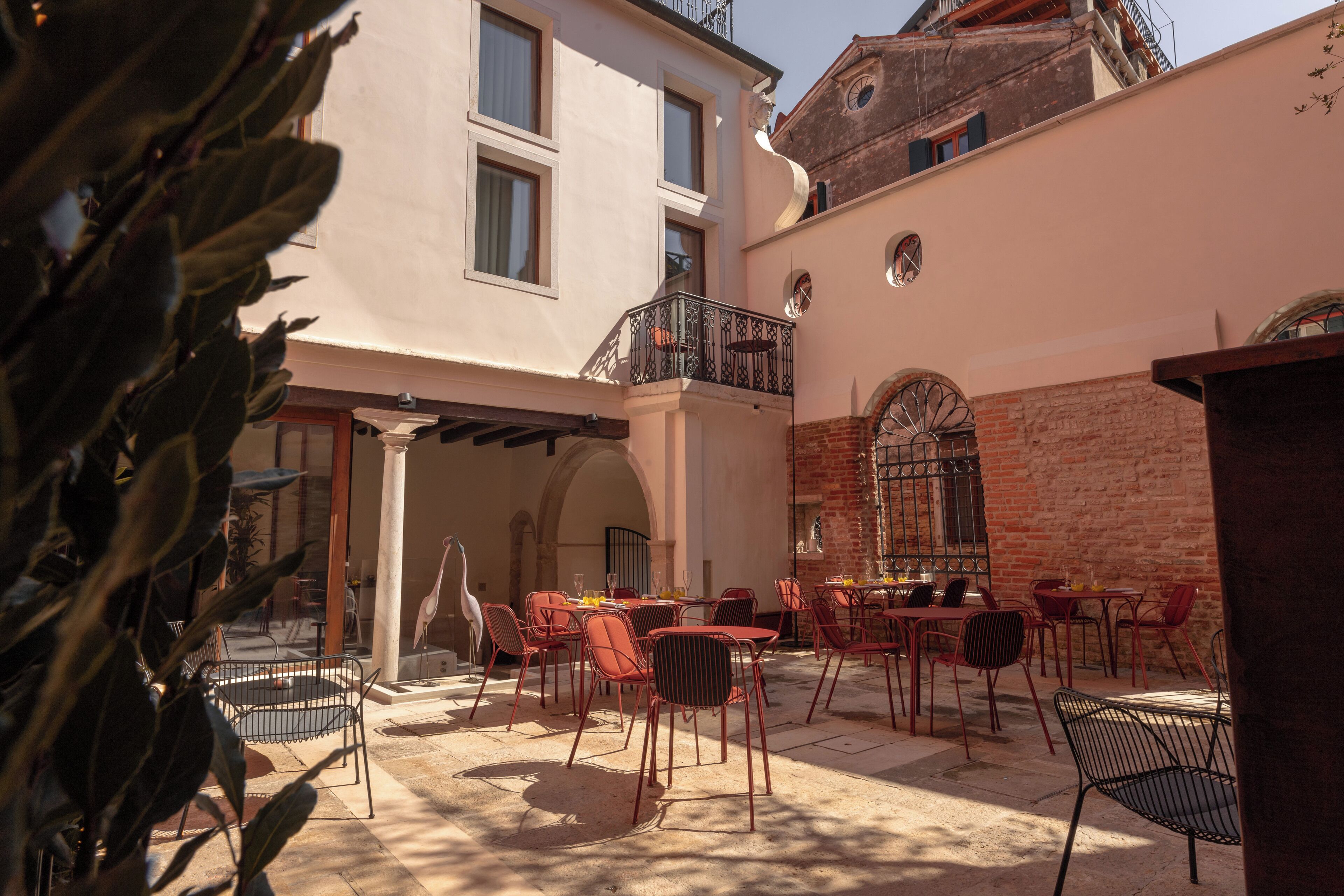 An outdoor seating area with tables and chairs, a brick wall, and a balcony.