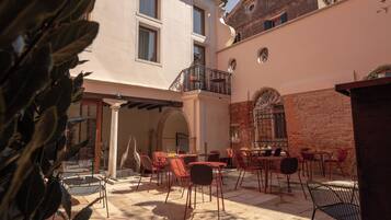 An outdoor seating area with tables and chairs, a brick wall, and a balcony.