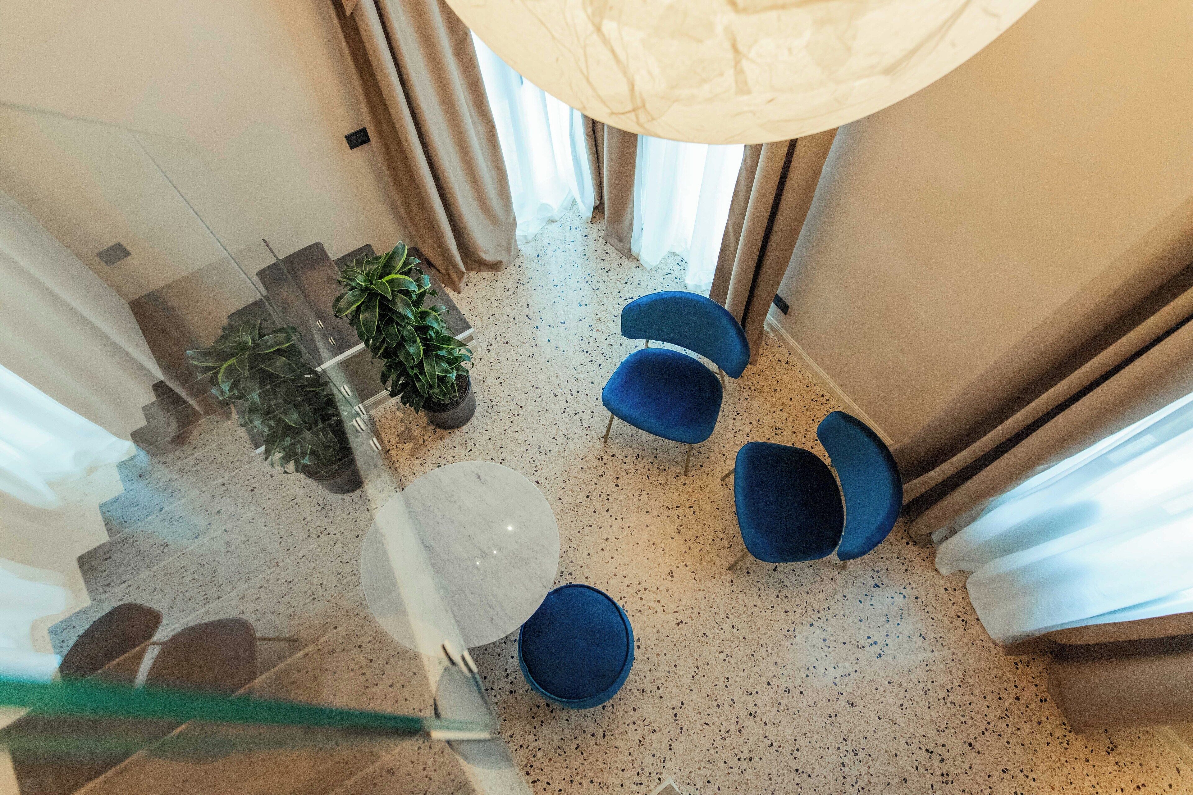 A modern interior with a glass railing, a marble table, blue chairs, and potted plants.