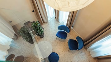 A modern interior with a glass railing, a marble table, blue chairs, and potted plants.