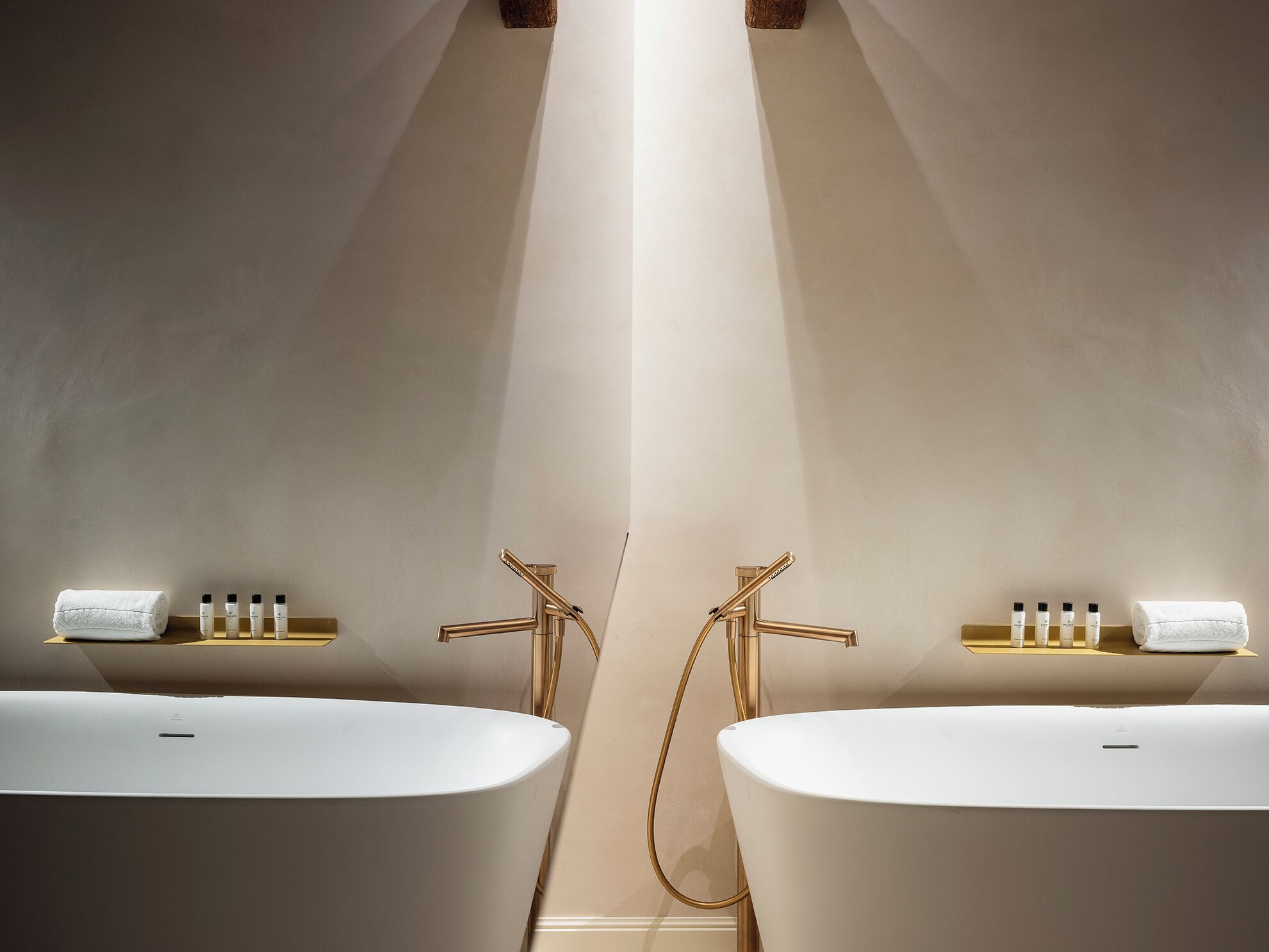 A modern bathroom with two white freestanding tubs, gold fixtures, and a central column.