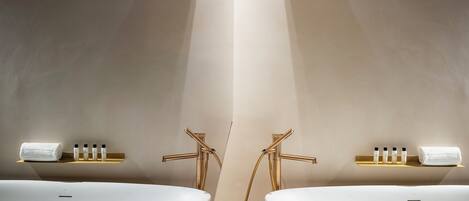 A modern bathroom with two white freestanding tubs, gold fixtures, and a central column.